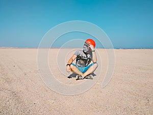 Young man sits thoughtfully in the middle of desert wearing a helmet for buggy.