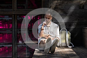 Young man sits on wooden stairs outdoors writing notes in paper pad in rays of sunlight