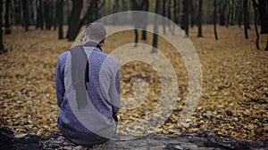 Young man sitting alone in autumn park, feels depression, nostalgia, loneliness
