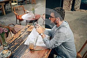 Young man sitting alone in cafe, using smarphone and listening on earphones photo