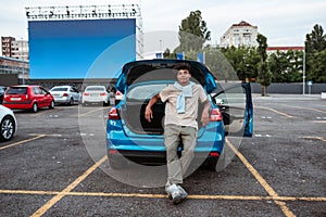 Young man sitting alone in open car trunk at autocinema