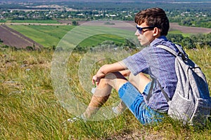 Young man sitting with backpack and looking at beautiful view, tourism concept