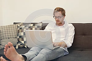 Young man sitting barefoot on couch with laptop