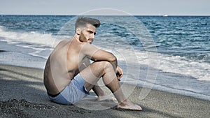 Young man sitting on a beach alone and lonely