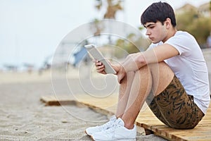 Young man sitting on beach holding tablet