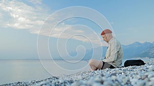 A young man sitting on the beach and working on a laptop