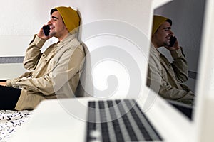 Young man sitting on the bed laughing while talking on the phone