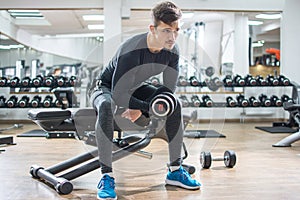 Young man sitting on bench and lifting weights in gym