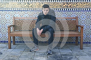 Young man sitting on a bench with ornaments in the background