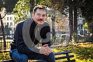 The young man is sitting on the bench in the park in Rome.