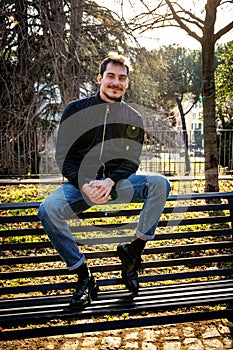 Young man is sitting on the bench in the park in Rome.