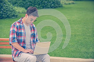 Young man sitting on bench in the park and working on laptop out