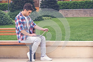 Young man sitting on bench in the park and working on laptop out