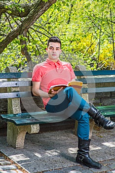Young man sitting on bench by tree in New York City, reading book