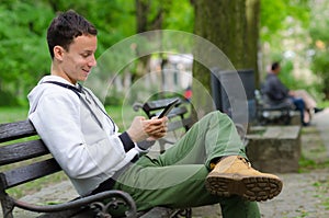 Young man sitting on the bench and using tablet device on beautiful spring day