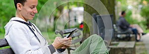 Young man sitting on the bench and using tablet device on beautiful spring day