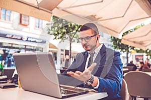 Young man sitting at cafe having a conversation on a laptop  wearing a headphones on head talking looks angry