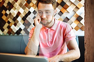 Young man sitting in cafe with laptop and phone, working, shopping online, hipster