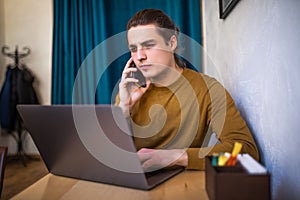 Young man sitting at a cafe table using laptop and talking on mobile phone. Handsome male sitting at restaurant and working