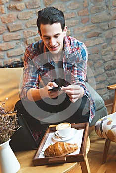 Young man sitting at a cafe, taking a snapshot of his food