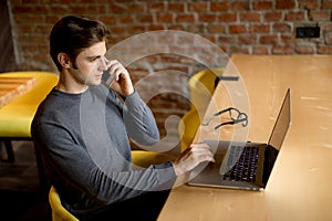 Young man sitting in cafe and using laptop and mobile phone