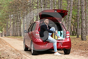 Young man sitting in car trunk loaded with suitcases