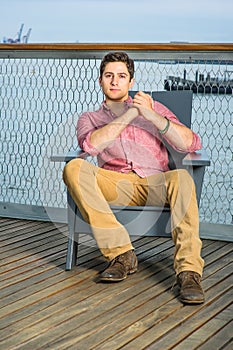 Young man sitting on a chair in the deck by the river, relaxing