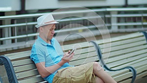 Young man sitting on a city bench with a mobile phone in his hands, camera tracking