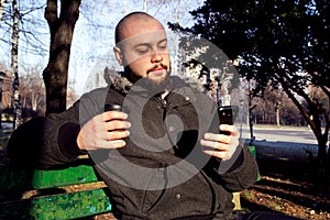 Young man sitting in city park with smart phone and drinking