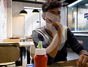 Young man sitting in a coffee shop sadly with a bottle of ketchup