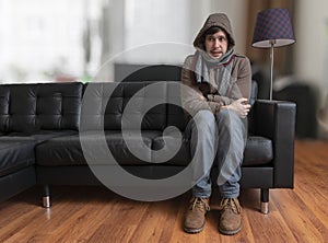 Young man sitting on couch is feeling cold at home.