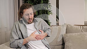 Young man sitting on the couch at home feeling bad heart problems heart attack.