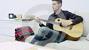 Young man sitting on a couch and playing guitar