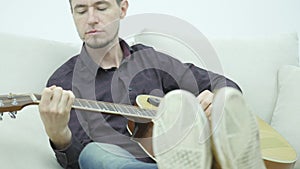 Young man sitting on a couch and playing guitar