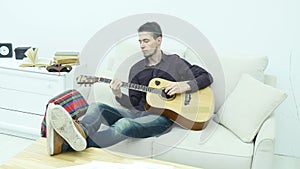 Young man sitting on a couch and playing guitar