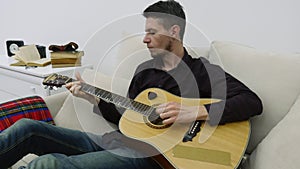 Young man sitting on a couch and playing guitar