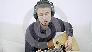 Young man sitting on a couch and playing guitar