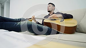 Young man sitting on a couch and playing guitar