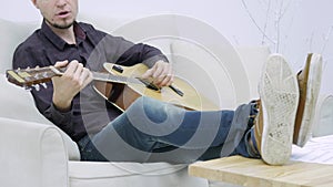 Young man sitting on a couch and playing guitar