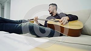 Young man sitting on a couch and playing guitar