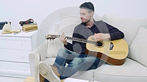 Young man sitting on a couch and playing guitar