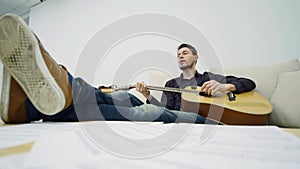 Young man sitting on a couch and playing guitar