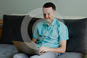 Young man sitting on the couch, thinking and working on laptop