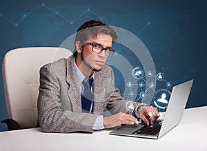 Young man sitting at desk and typing on laptop with social network icons