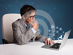 Young man sitting at desk and typing on laptop with social network icons