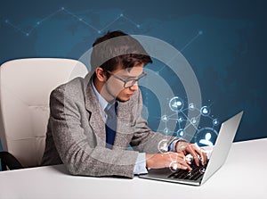 Young man sitting at desk and typing on laptop with social network icons