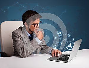 Young man sitting at desk and typing on laptop with social network icons