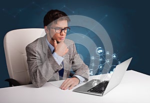 Young man sitting at desk and typing on laptop with social network icons