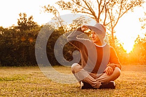 Young man sitting down on the green grass, enjoying a sunset relaxation in a park. Concept of freedom relaxation. Place for text