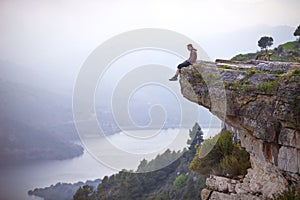 Young man sitting on edge of cliff and looking at river